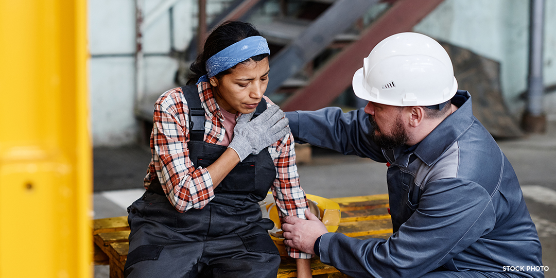 A construction worker helping their female colleague with her injured shoulder.