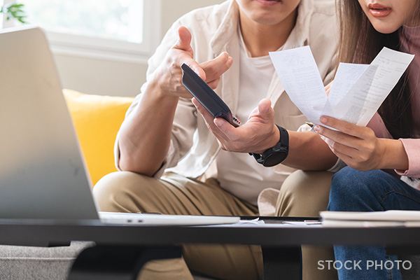 A couple frustrated over workers' comp documents & a calculator look at their laptop computer.